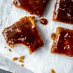 five caramel blondies with flaky sea salt on parchment paper on top a grey slate with one bite taken out of the bottom left blondie