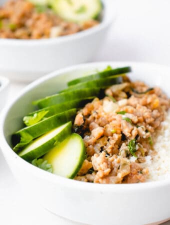 two white bowls with sliced cucumber, ground pork and finely chopped cauliflower