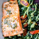 wide and shallow white bowl with kale, roasted vegetables, a fillet of roasted salmon on the left side and a drizzle of avocado cilantro lime sauce
