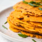 light brown speckled plate with a stack of sweet potato tortillas and sliced green onions