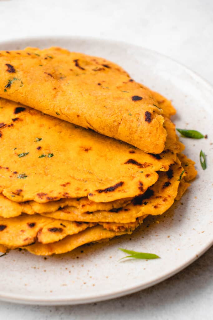 light brown speckled plate with a stack of sweet potato tortillas with the top tortilla folded in half sprinkled with chopped green onions