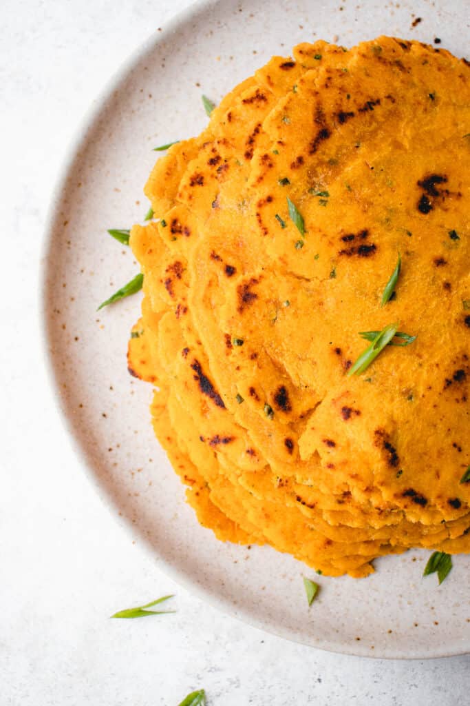 light brown speckled plate with a stack of sweet potato tortillas and sliced green onions 