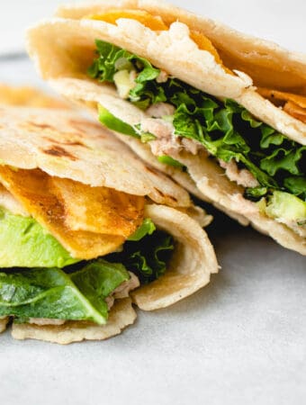 two cassava flour wraps stuffed with tuna salad, kale, avocado and plantain chips on a piece of parchment paper
