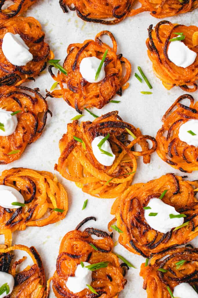 overhead shot of butternut squash latkes topped with a dollop of sour cream and chives on a white piece of parchment paper