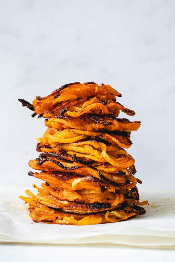 a stack of butternut squash latkes on a few pieces of parchment paper against a light grey background
