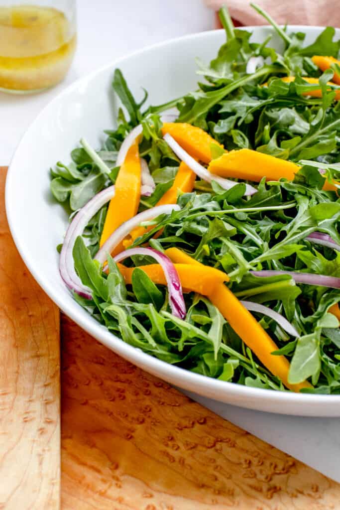 white flat bowl with arugula mango salad flanked by two large wooden salad spoons