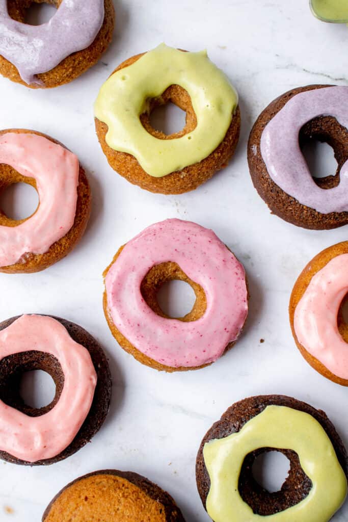a series of lavender, pink and green frosted chocolate and vanilla mini donuts against a marble backdrop