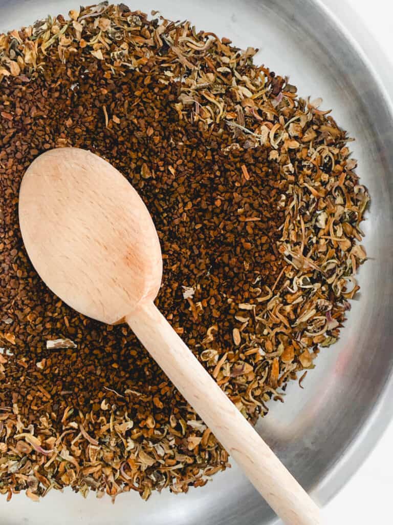 stainless steel skillet with dandelion and chicory grounds and a long wooden spoon