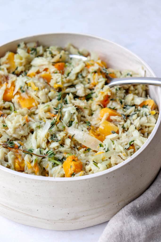 beige wide bowl with a serving spoon inside salted cod cooked in coconut milk with squash and thyme