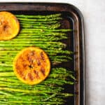 brown sheet pan with grilled asparagus spears topped with sliced, grilled oranges on a light brown background