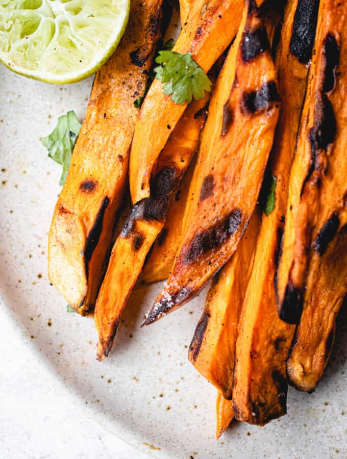grilled sweet potato wedges on a light beige speckled plate garnished with chopped cilantro and a half a lime