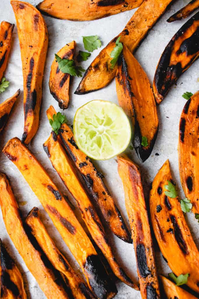 grilled sweet potato wedges on a white piece of parchment paper garnished with chopped cilantro and a half a lime