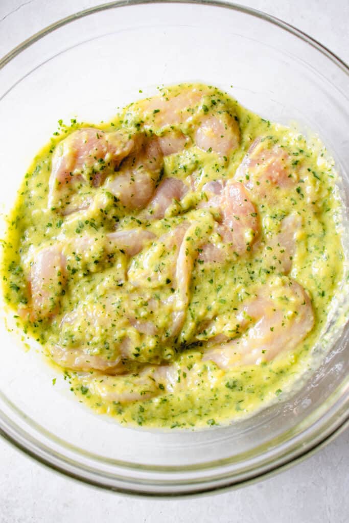 glass bowl with raw chicken breast strips covered in cilantro, mango and lime marinade