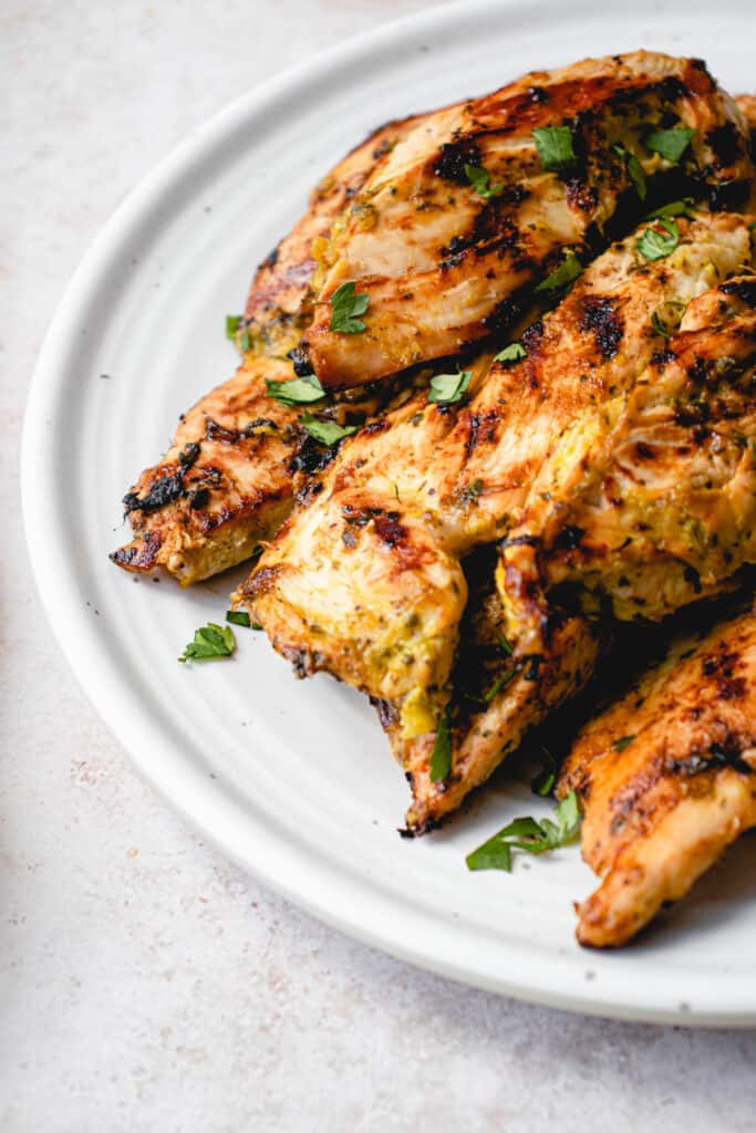 white plate with grilled chicken breast strops garnished with cilantro