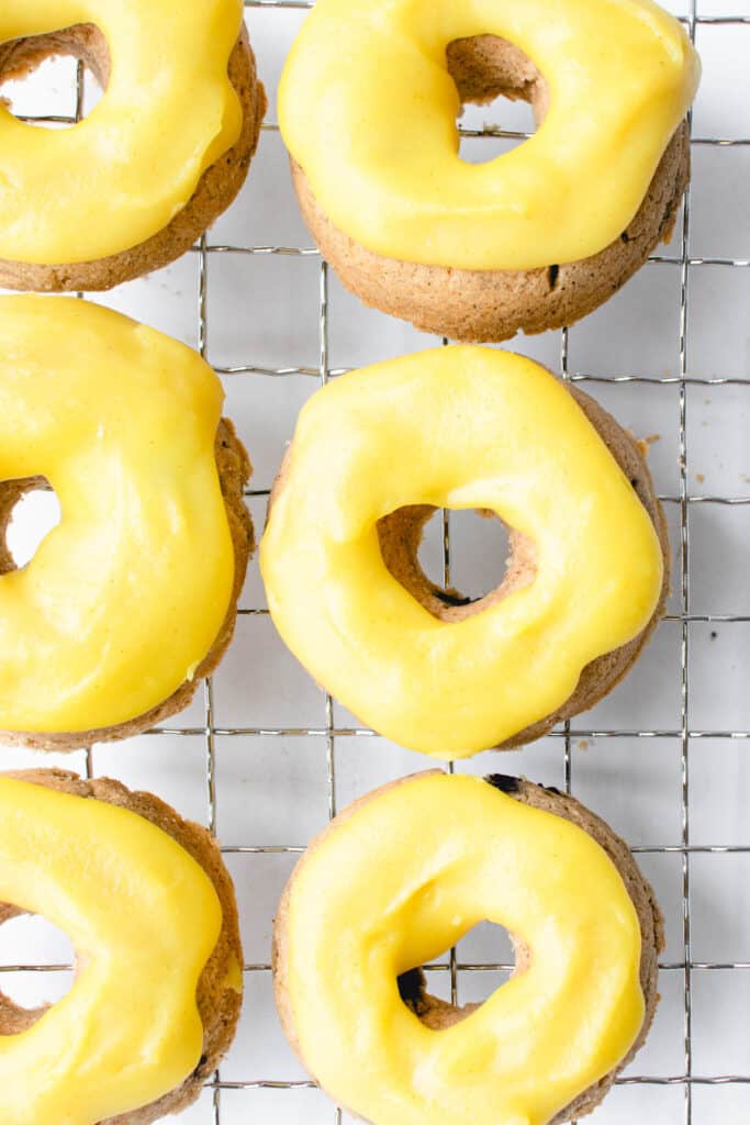 six mini blueberry donuts with a bright yellow glazed arranged vertically in two rows of three on a metal cooling rack against a white background