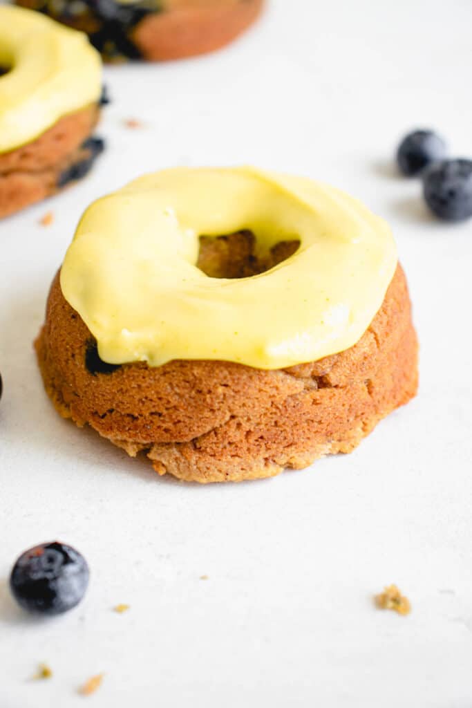 three mini donuts on a white backdrop garnished with a thick lemon yellow colored glaze and a few scattered blueberries