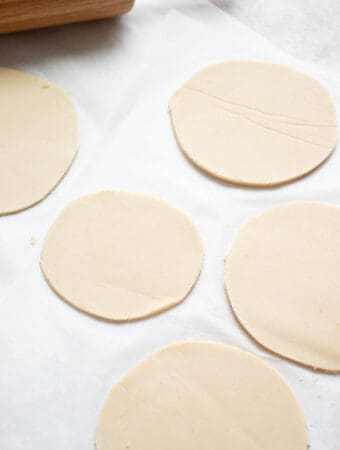 four circles of rolled out dough with a light brown rolling pin on a white piece of parchment paper