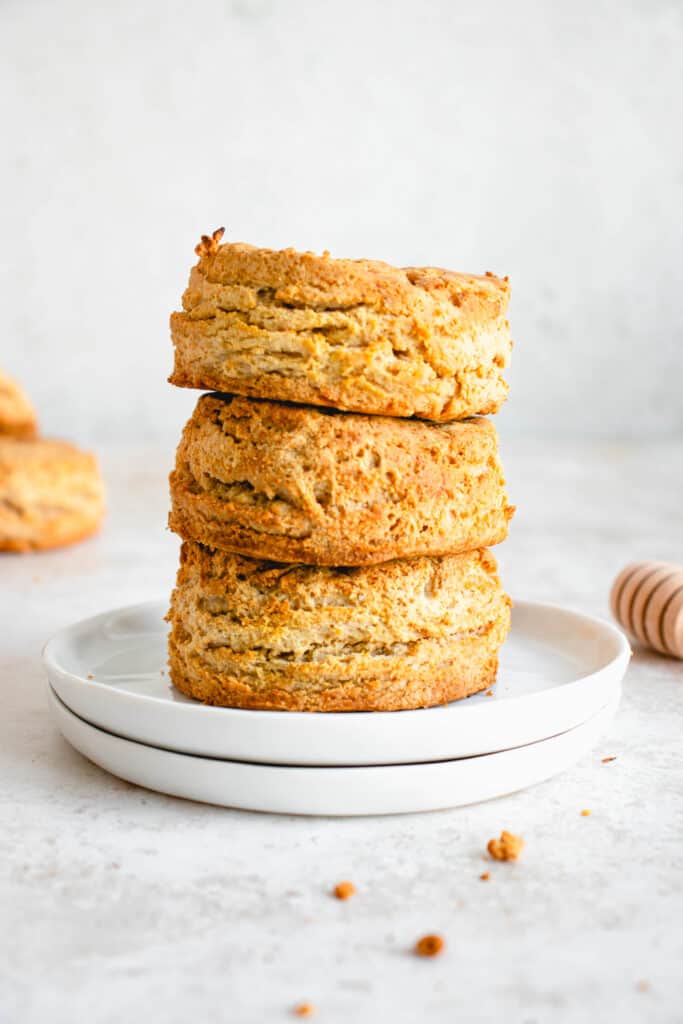 stack of three butternut squash biscuits on two stacked white plates with swizzle stick to the right of the plates and two biscuits in the background to the left of the plate 