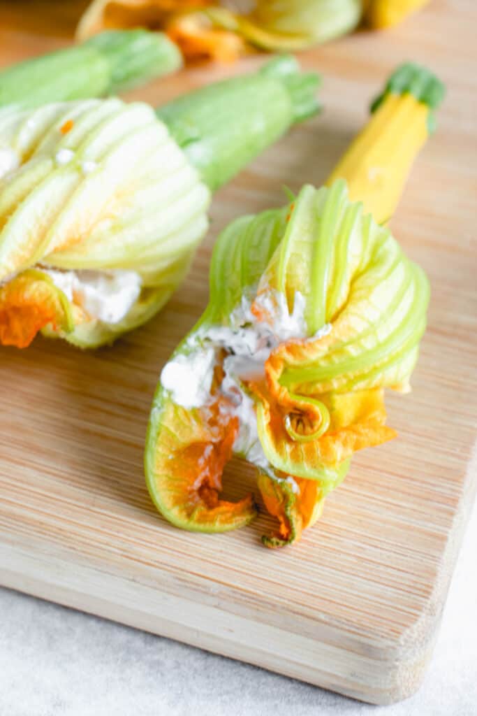 two zucchini blossoms stuffed with coconut yogurt, thyme, lemon zest and garlic on a light wooden cutting board