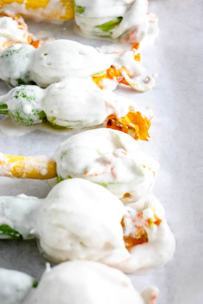 six zucchini blossoms covered in battered on a parchment lined baking sheet