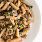 overhead shot of half of a white wide mouth bowl with penne, ground beef, spinach and portobello mushrooms