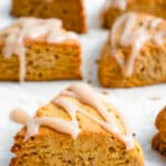 90 degree shot of sheet pan lined with a white piece of parchment paper with six pumpkin scones drizzled with maple spice icing