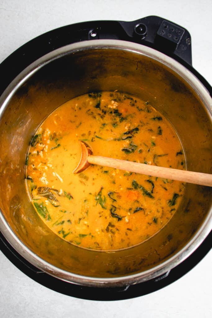 overhead shot of instant pot on a light beige table with pumpkin and chicken soup with a long wooden spoon placed inside the instant pot
