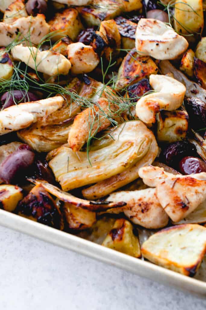 stainless steel sheet pan with chicken breast strips, kalamata olives, white sweet potatoes and pears garnished with fennel fronds