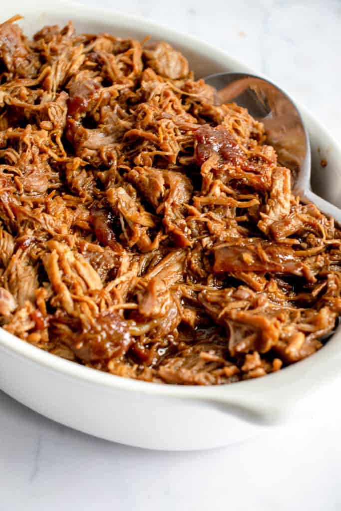 oval white casserole dish with bbq pulled pork and a large stainless steel serving spoon 