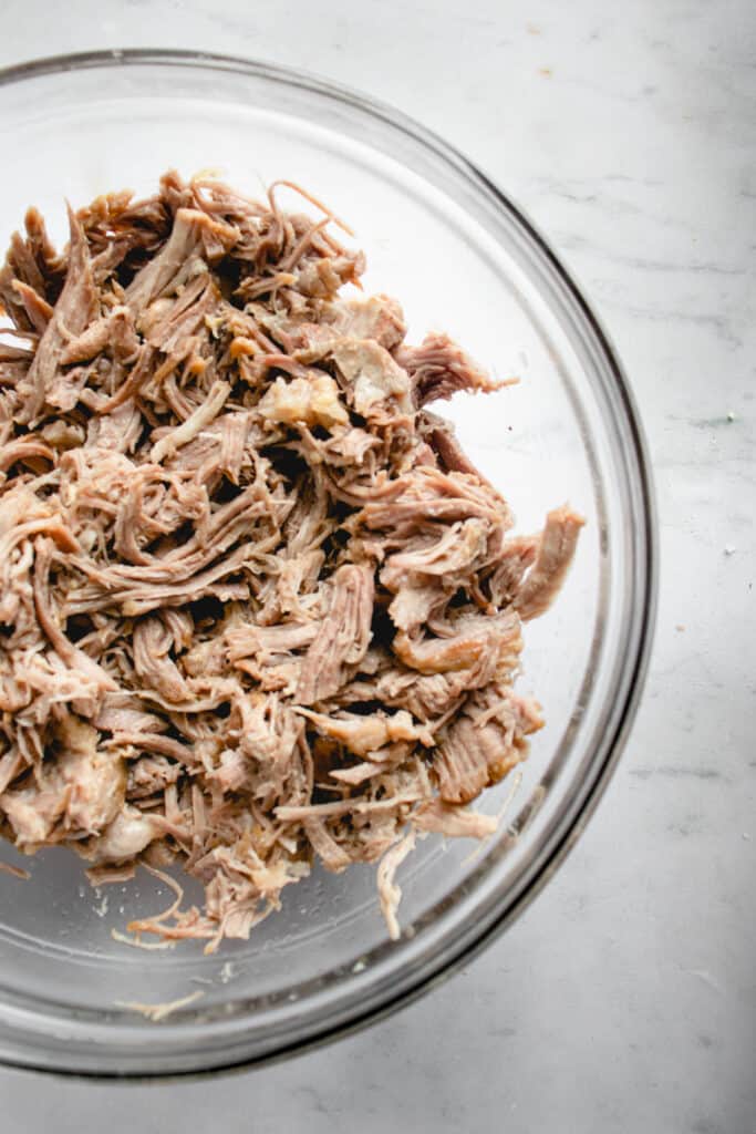 clear glass bowl with shredded pork on a marble white, grey and blue tabletop