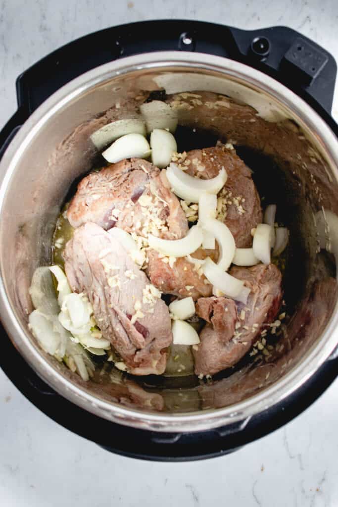 overhead shot of instant pot with seared pieces of pork shoulder with onion and garlic