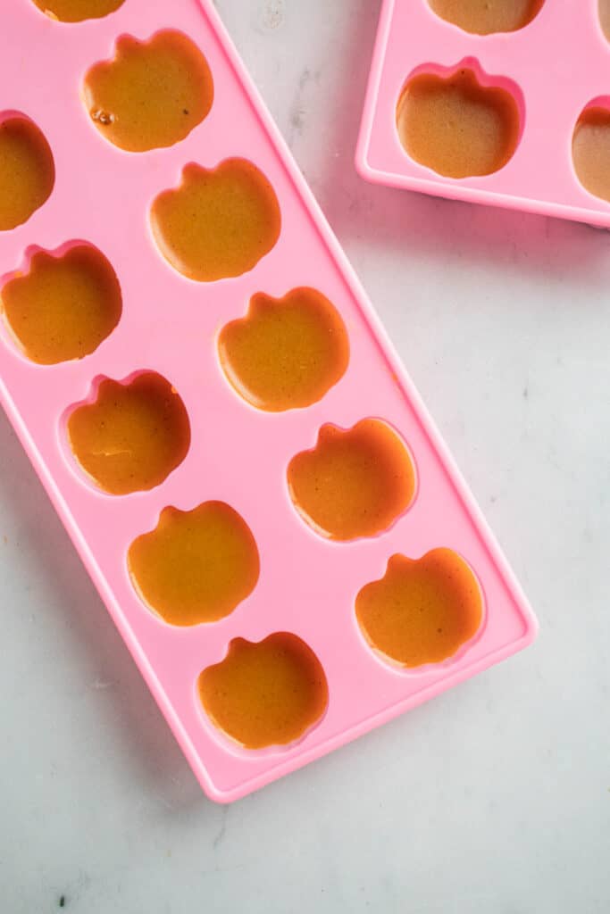 Two rectangular shaped pink silicone moulds with mini pumpkins, filled with orange pumpkin spice gummies
