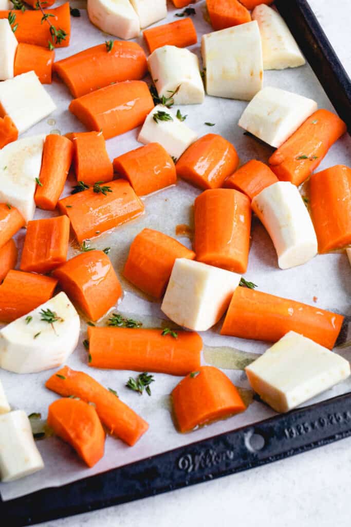 sheet pan lined with parchment paper and topped with chopped carrots and parsnips in olive oil sprinkled with fresh thyme