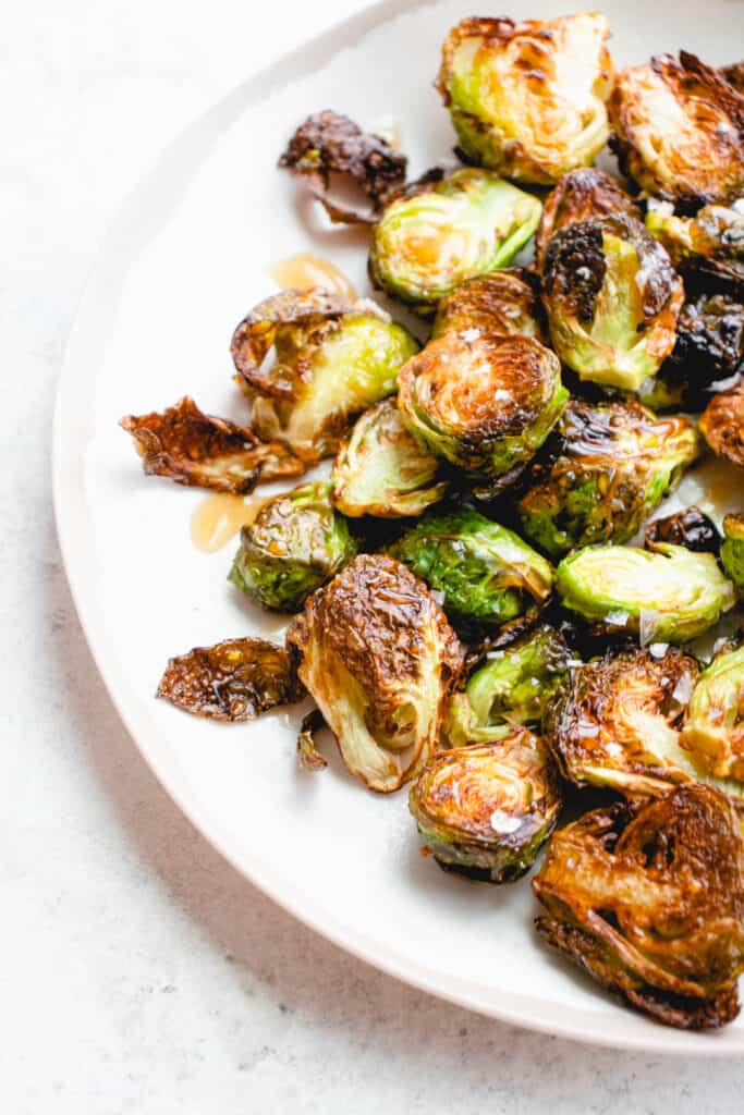 half of a white plate with a light brown rim with roasted brussels sprouts drizzled with a maple glaze and flaky sea salt