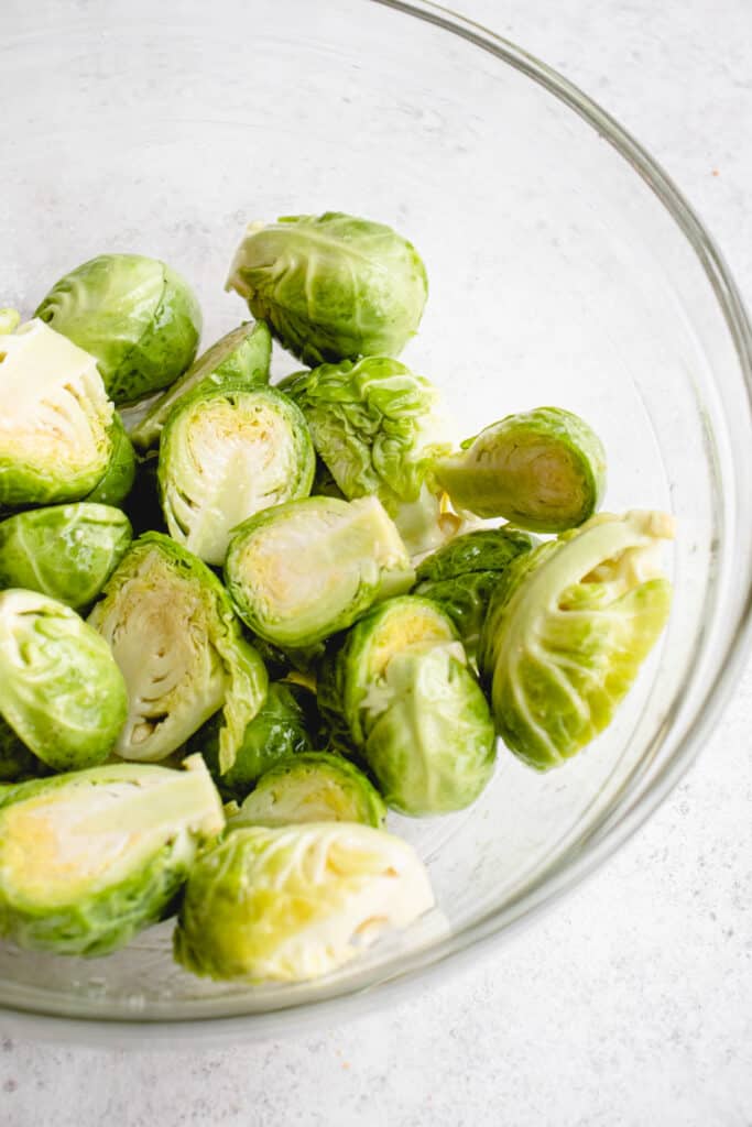 clear glass bowl with brussels sprouts sliced in half against a grey background