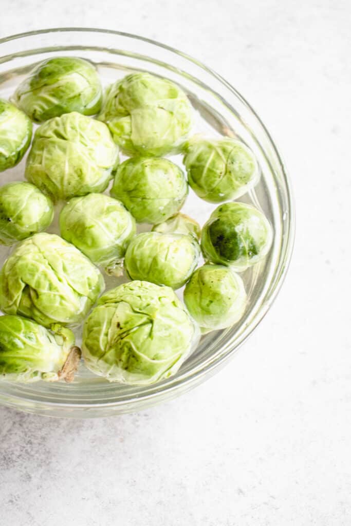 clear glass bowl with brussels sprouts sliced in half against a grey background
