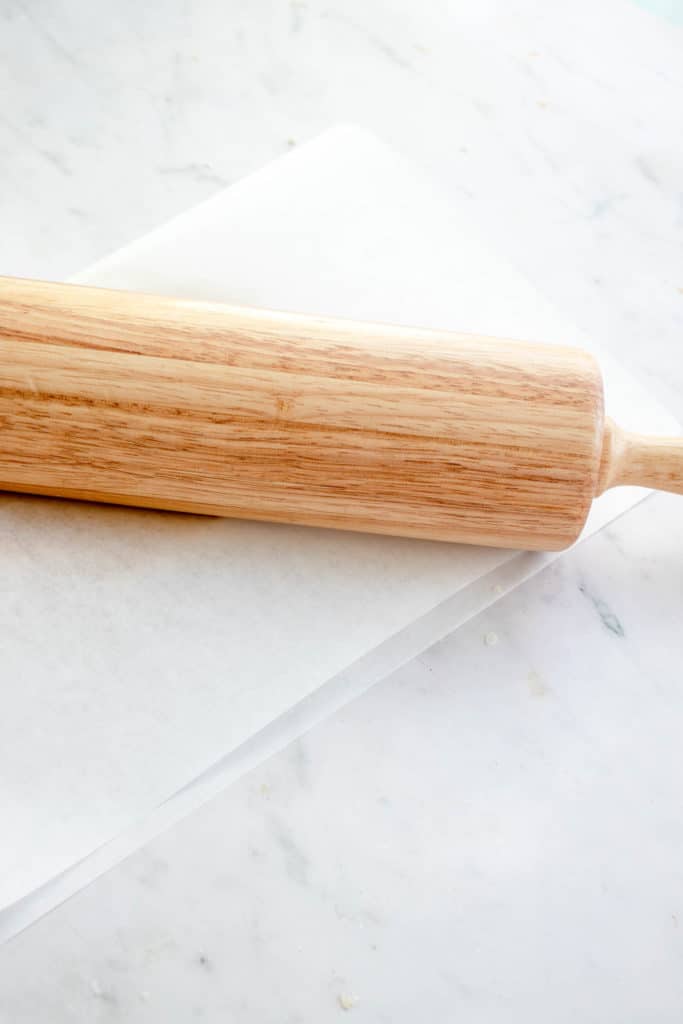 wooden rolling pin sitting on top a piece of parchment paper folded in half with a disc of pie crust inside.