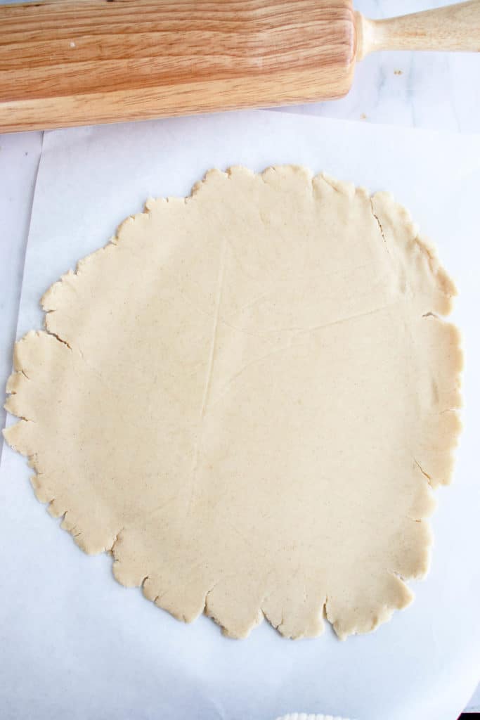 overhead shot of white piece of parchment paper with rolled out pastry dough and a wooden rolling pin