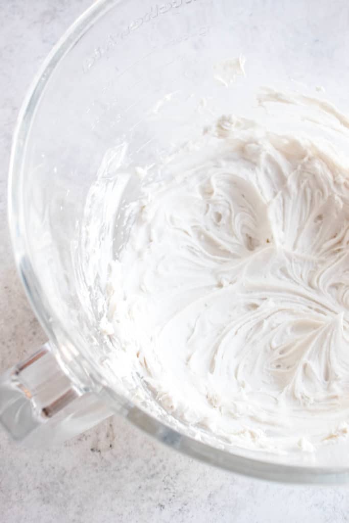 a clear glass mixing bowl with whipped coconut cream against a grey background