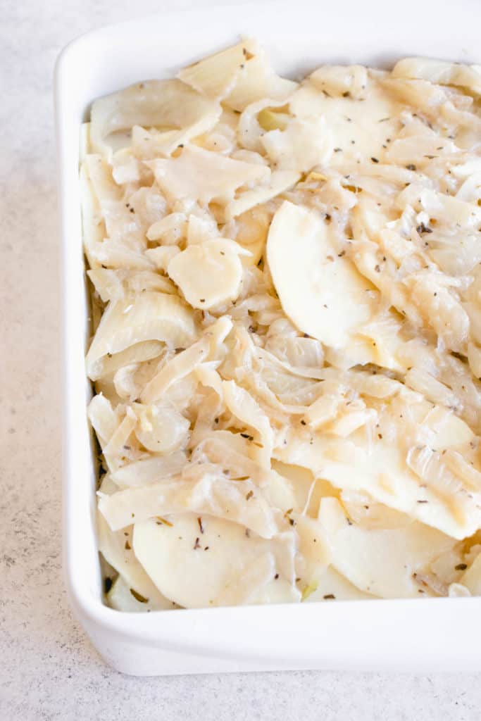 white casserole dish with sliced sweet white potatoes mixed with fennel, onion, dried herbs and a coconut cheese sauce