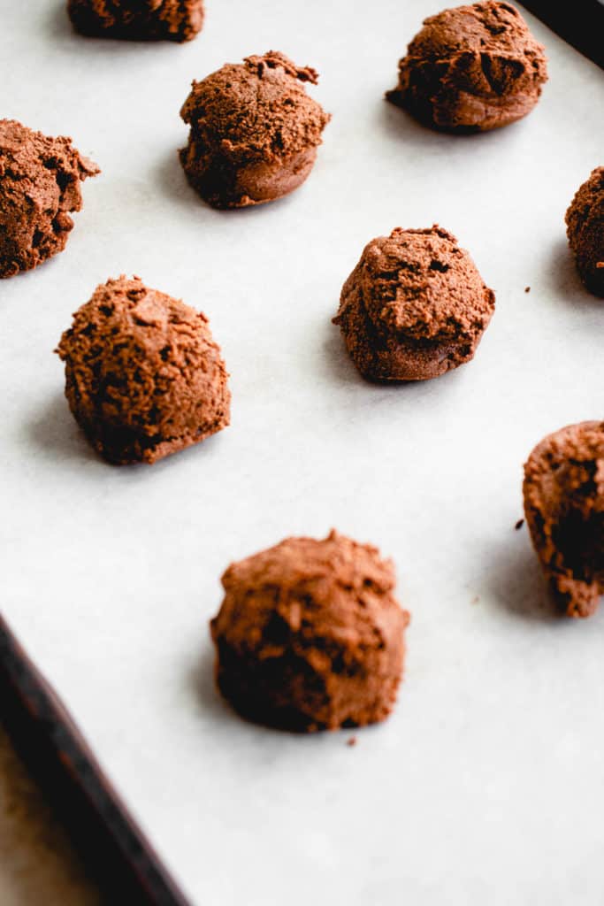 balls of chocolate peppermint cookie dough on a baking sheet with white parchment paper