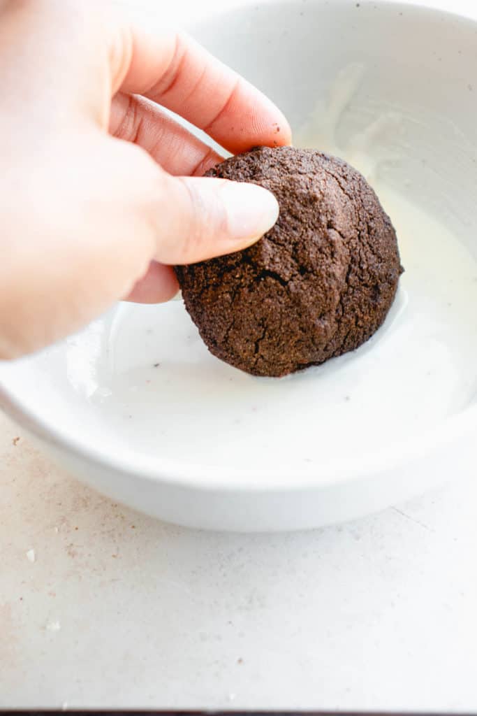 hand dipping chocolate cookie into white bowl filled with melted coconut butter