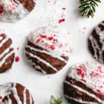 overhead shot of chocolate cookies half dipped in coconut butter and decorated with shredded coconut and freeze dried raspberries on a white background with decorative pine tree leaves