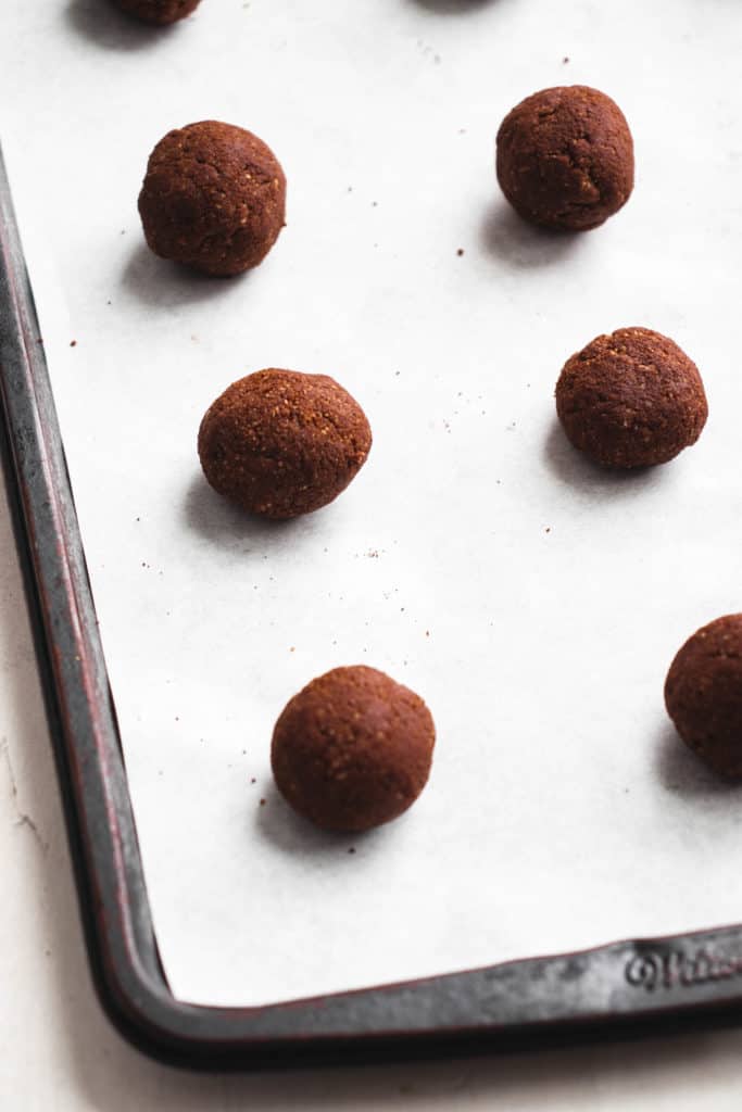 dark sheet pan with white parchment paper and balls of chocolate cookie dough