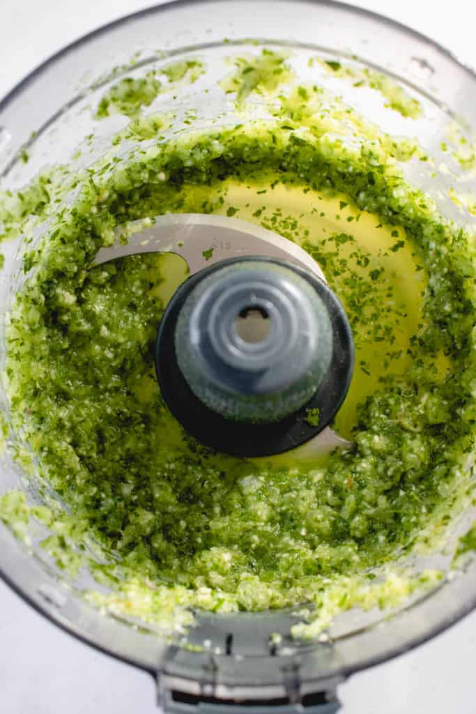 overhead shot of food processor with green seasoning made of garlic, onions, green onions, thyme and culantro