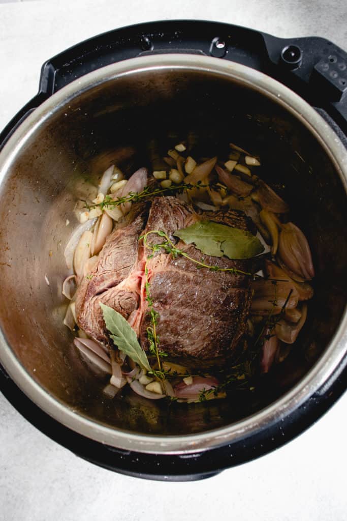 overhead shot of instant pot with seared beef chuck roast, shallots, garlic, two bay leaves and sprigs of thyme