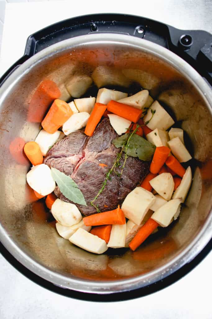 overhead shot of instant pot with seared beef chuck roast, white sweet potatoes, chopped carrots, two bay leaves and sprigs of thyme