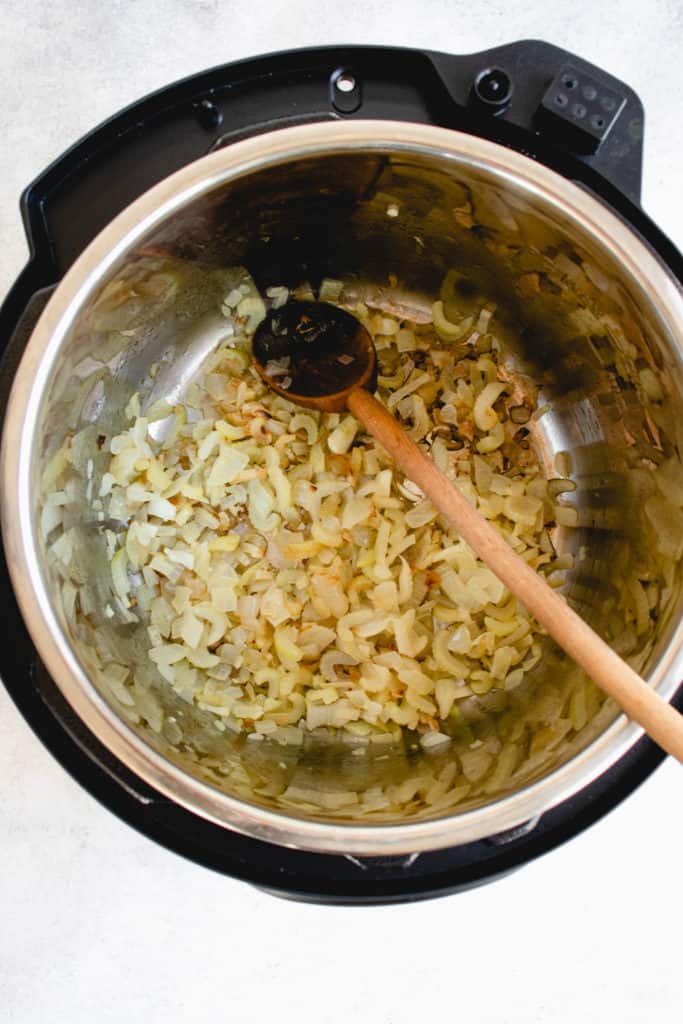 overhead shot of Instant Pot with sauteed celery, onions and garlic with a long light wooden spoon