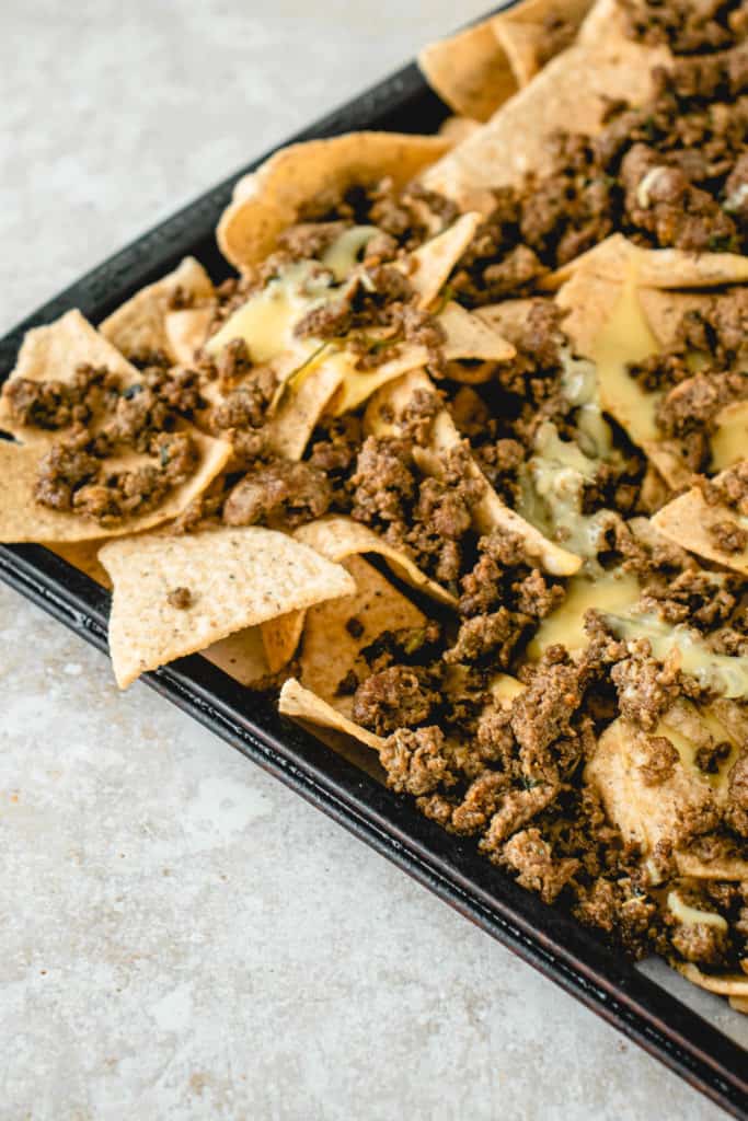 sheet pan with grain free tortilla chips, dairy-free nacho cheese and ground beef AIP taco meat on a beige speckled backdrop
