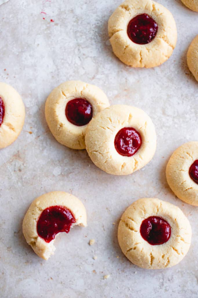 overhead shot of paleo thumbprint cookies with a berry filling. there is a bite taken out of one of the cookies with a few scattered crumbs